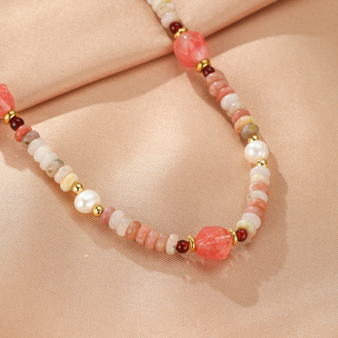 Collier artisanal avec perles de rhodonite roses et blanches, perles d'eau douce et accents dorés, sur fond rose poudré.