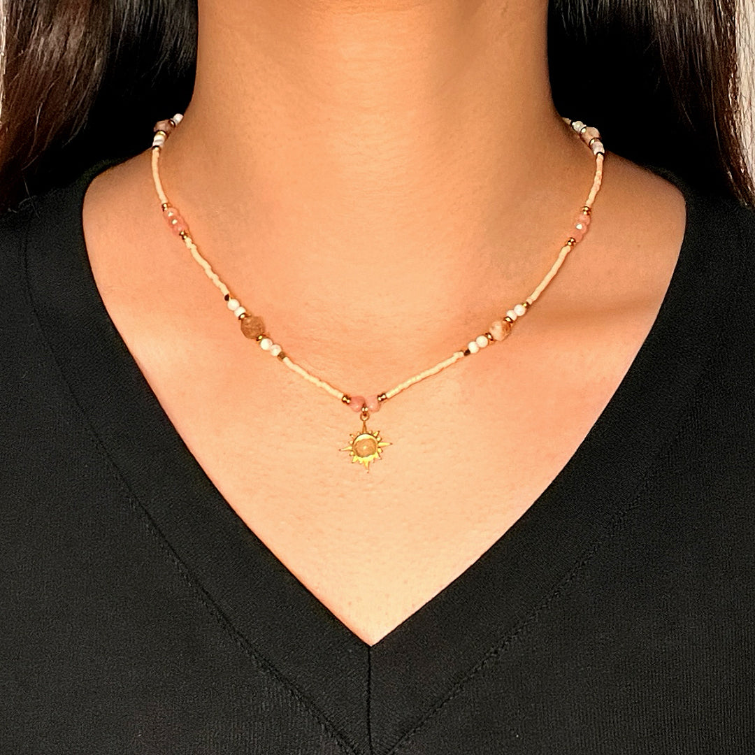 Collier d'été fait à la main avec des perles beiges, roses et blanches, orné d'un pendentif soleil doré au centre.