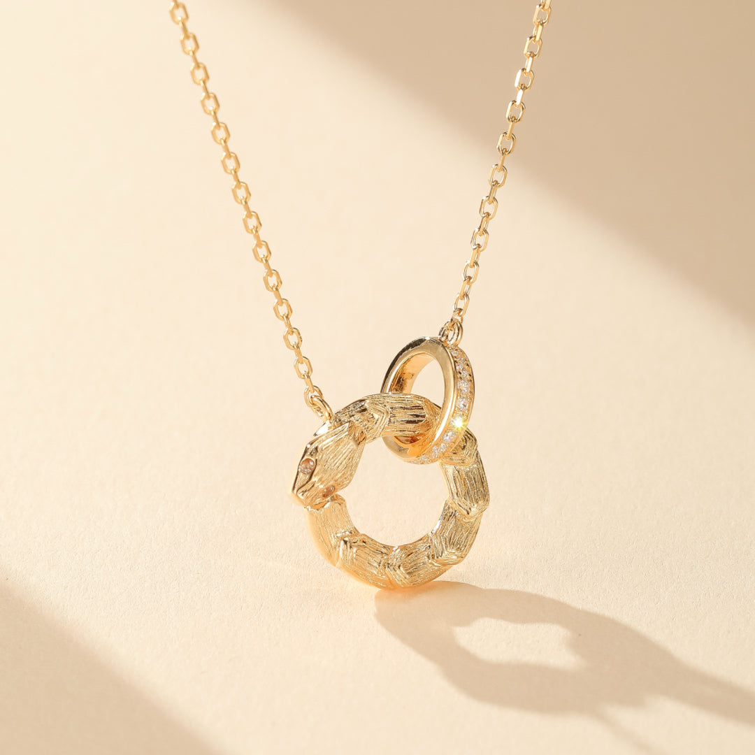 Collier Serpent avec un pendentif en forme d'anneau orné de petits zirconiums et un autre anneau texturé imitant un serpent en argent plaqué or.