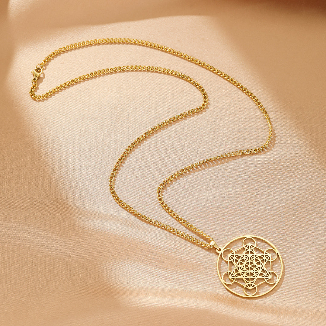 Collier plaqué or avec un pendentif circulaire représentant la géométrie sacrée du Sri Yantra, sur un fond satiné beige.