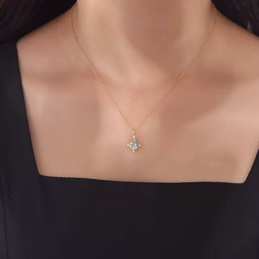 Un collier délicat en argent 925 avec une pierre topaze bleue centrale entourée de petits diamants scintillants, le tout monté sur une chaîne fine en or jaune.