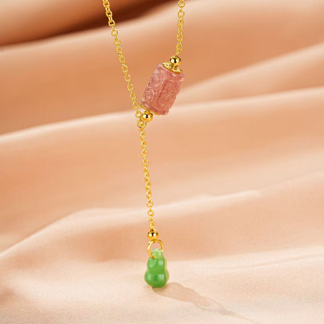 Collier en or jaune avec pendentif en forme de gourde en jade vert et un cylindre en tourmaline rose sculpté, sur fond de tissu satiné rose.