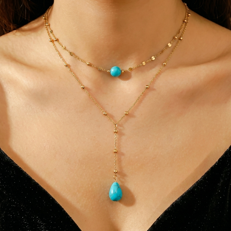 Collier double chaîne plaqué or avec une pierre turquoise ronde sur la chaîne supérieure et une pierre turquoise en forme de goutte sur la chaîne inférieure.