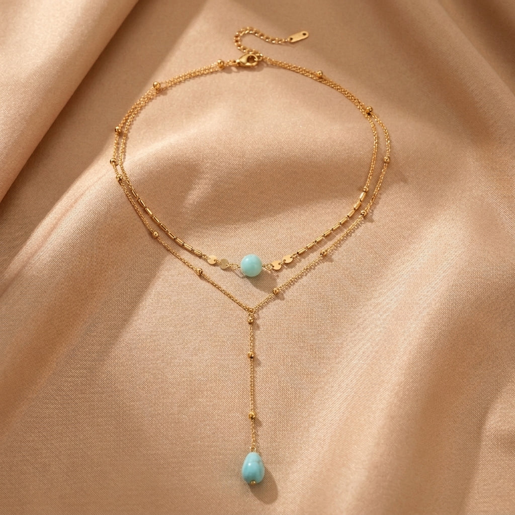 Collier plaqué or avec deux chaînes superposées, ornées de perles et de pierres turquoise naturelles en forme de goutte et de boule.
