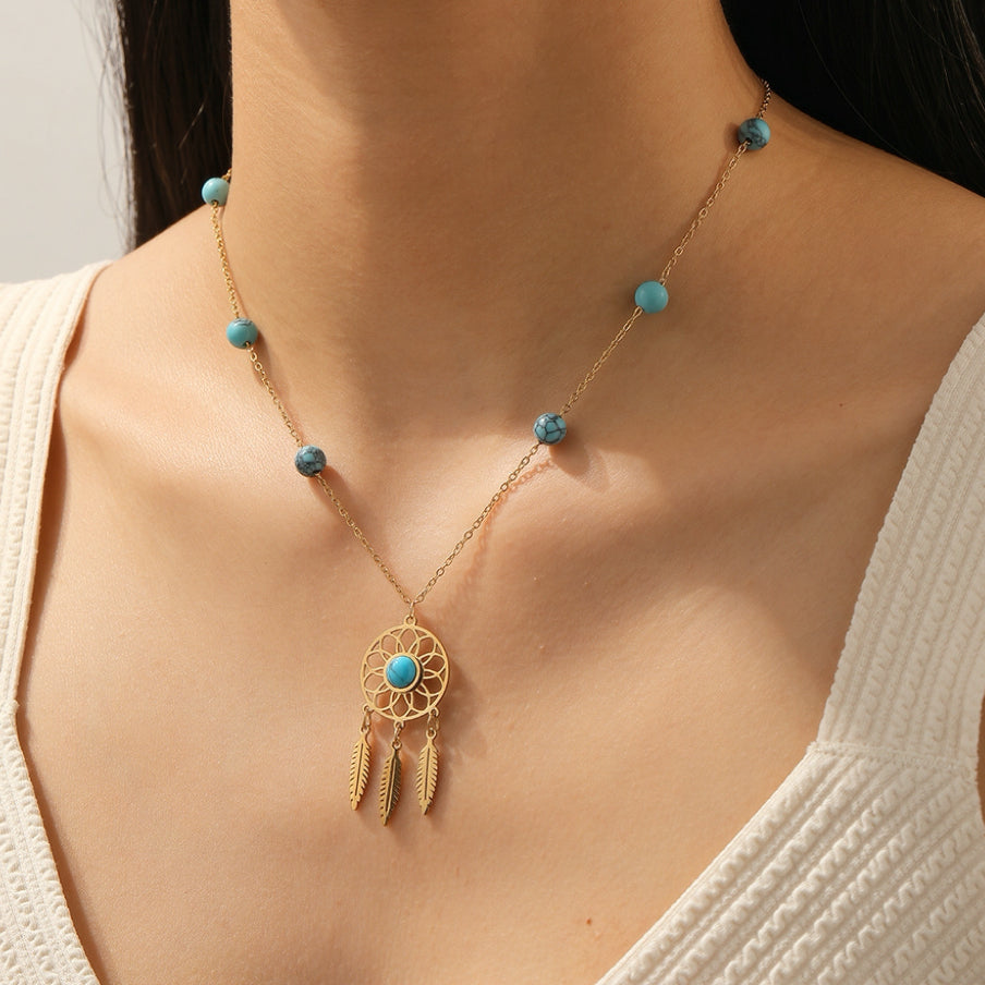Collier doré avec un pendentif attrape-rêves orné d'une turquoise et de trois plumes, rehaussé de perles turquoises sur la chaîne.