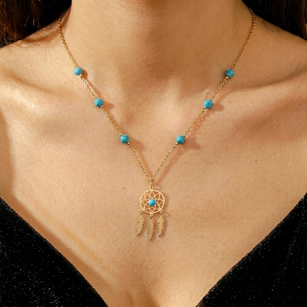 Collier doré avec un pendentif attrape-rêves orné de petites perles turquoise et de plumes, inspiré de l'Esprit d’Oasis.