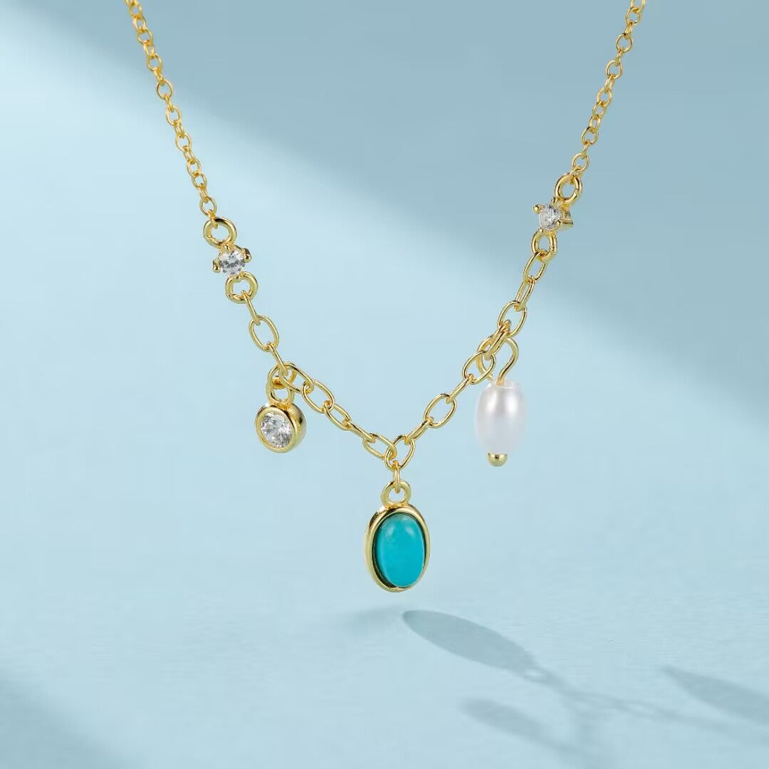 Collier en argent plaqué or avec une chaîne à maillons, orné d'une turquoise ovale, d'une perle blanche et de deux cristaux scintillants.
