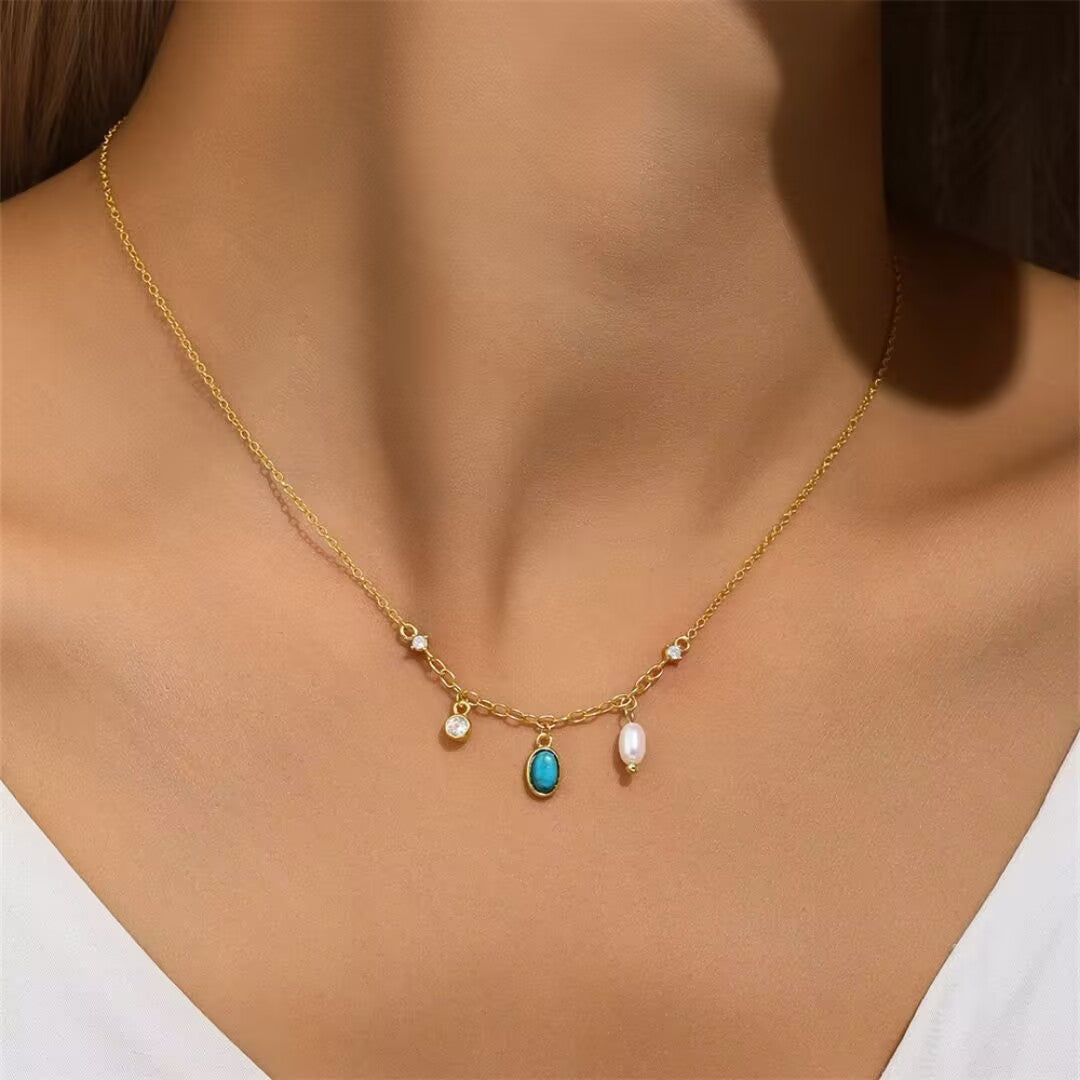 Collier fin en argent plaqué or avec pendentif turquoise ovale et perle blanche, orné de petites pierres scintillantes.