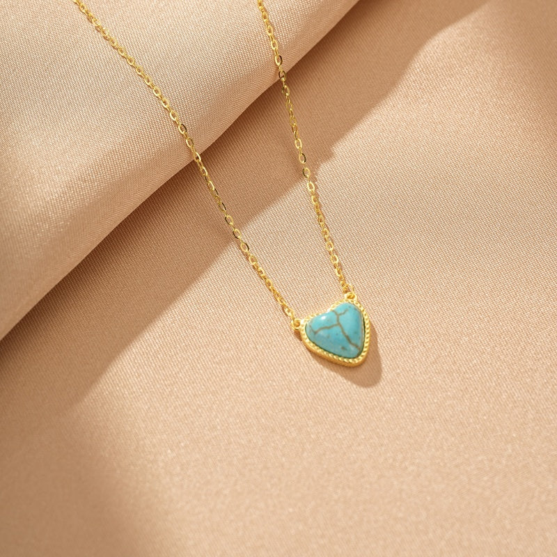 Collier en argent plaqué or avec un pendentif en forme de cœur en turquoise bleue, sur fond beige.