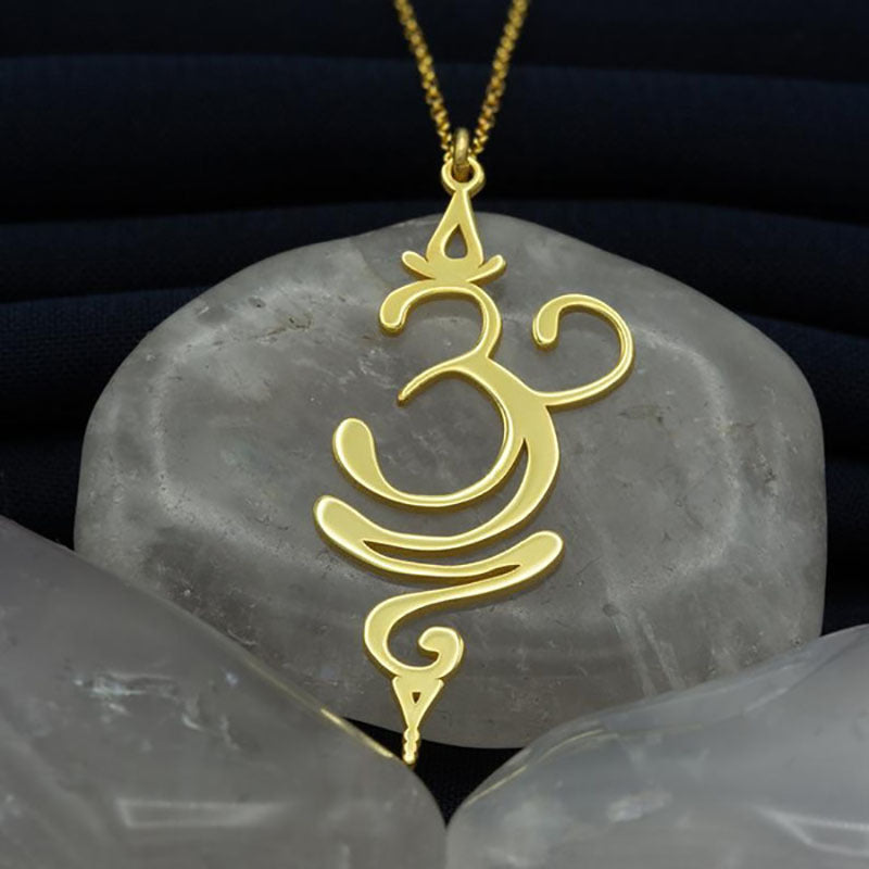Pendentif Unalome en or, symbole de confiance, posé sur des pierres grises
