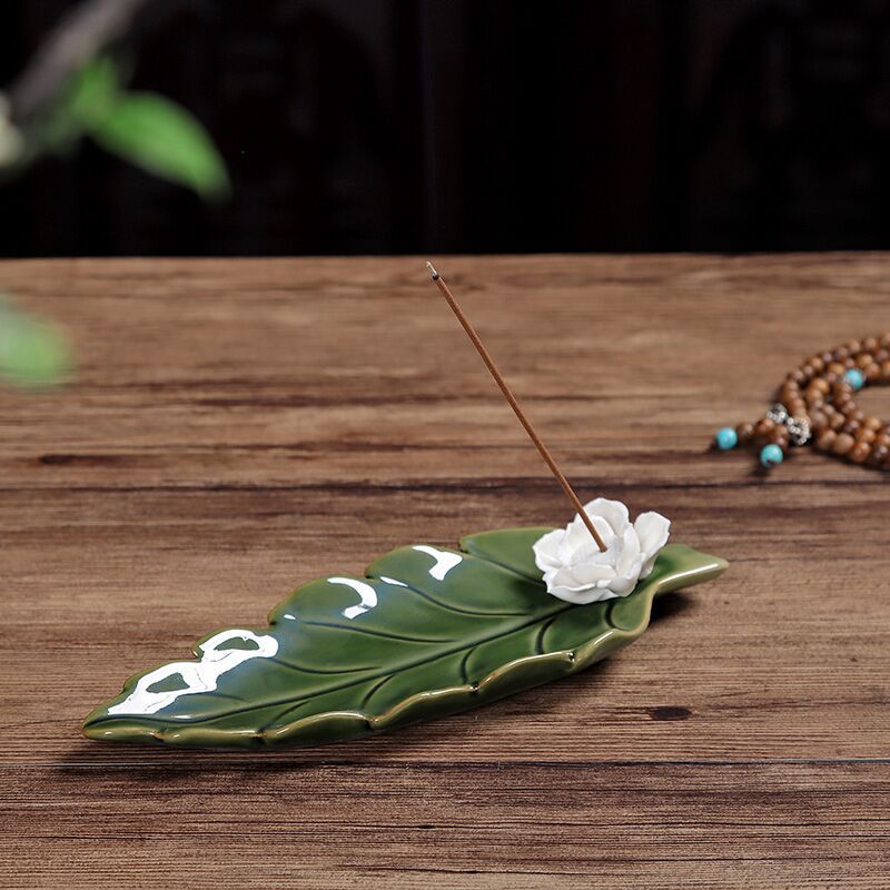 Encensoir "Fleur de Lotus" en céramique verte avec une fleur blanche décorative et un bâton d'encens allumé.
