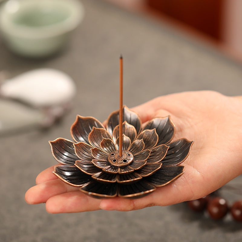 Un encensoir en métal en forme de fleur de lotus tenant un bâton d'encens allumé, tenu dans une main.