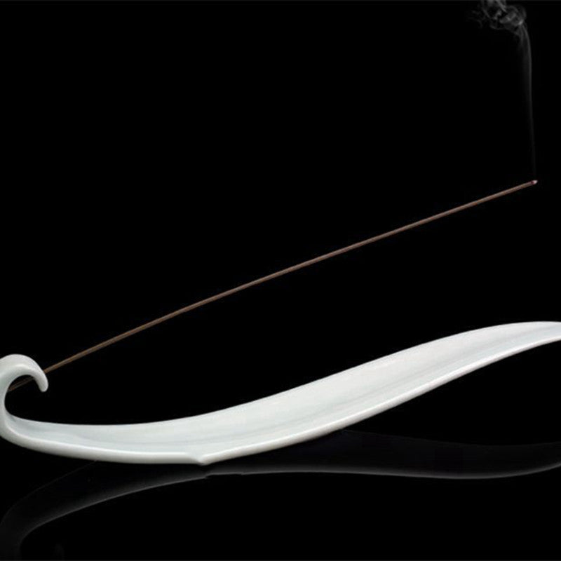 Encensoir "Vague" en céramique blanche, avec un bâton d'encens allumé et fumée légère, sur fond noir.