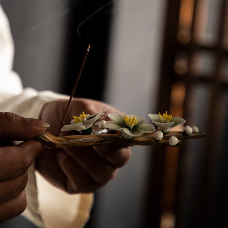 Encensoir Zen fait main en céramique avec des fleurs blanches et des perles, une tige d'encens allumée dégageant de la fumée.