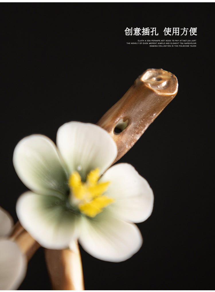 Encensoir zen en céramique blanche et verte avec une fleur délicate et un support en bois, sur fond noir.