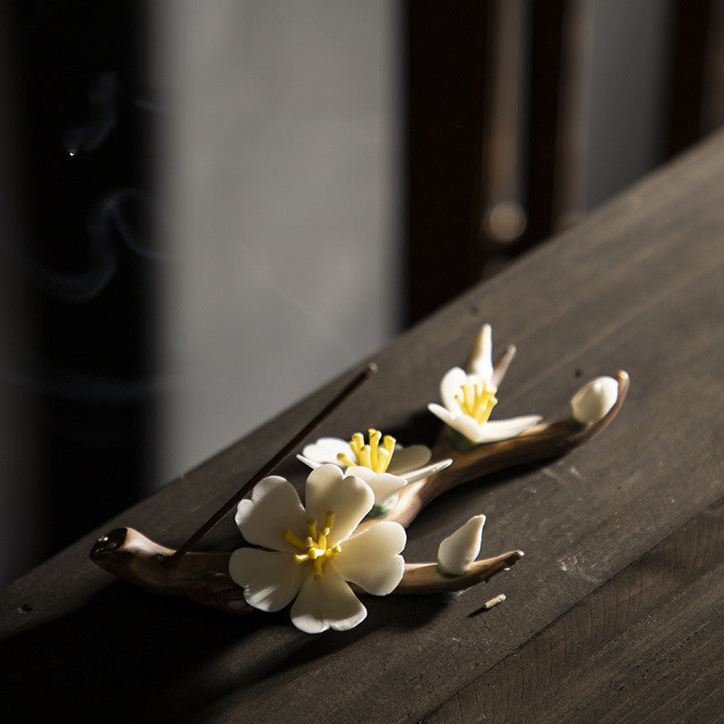Encensoir zen en céramique fait main, décoré de fleurs de prunier blanches et d'un bâton d'encens allumé dégageant de la fumée.