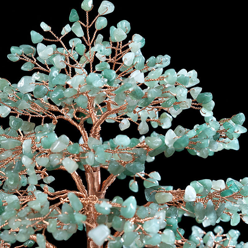 Gros plan sur un arbre de vie artisanal avec des pierres vertes d'aventurine et un tronc en fil de cuivre torsadé, sur fond noir.