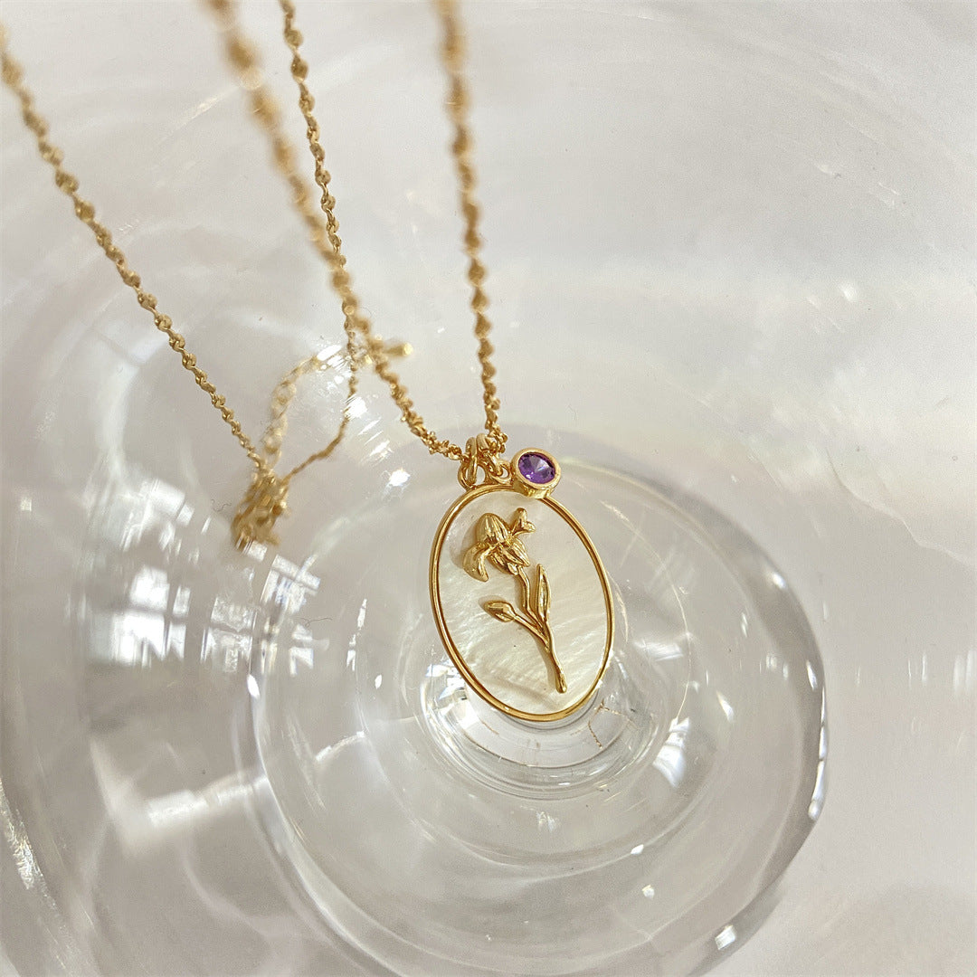 Pendentif en or avec une pierre de naissance iris pour le mois de février sur un fond nacré.