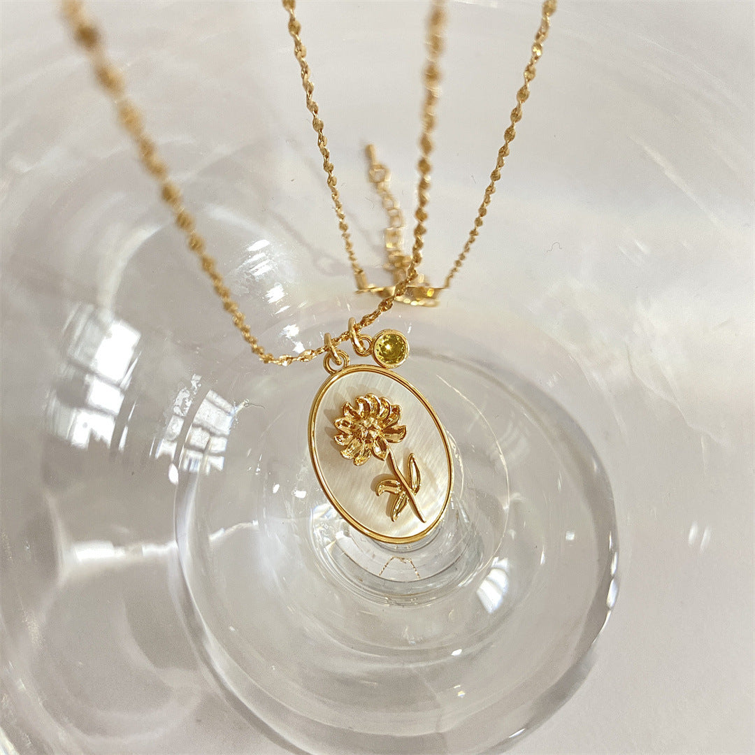 Pendentif Romance en or avec une fleur de chrysanthème dorée sur fond nacré, orné d'une petite pierre jaune.