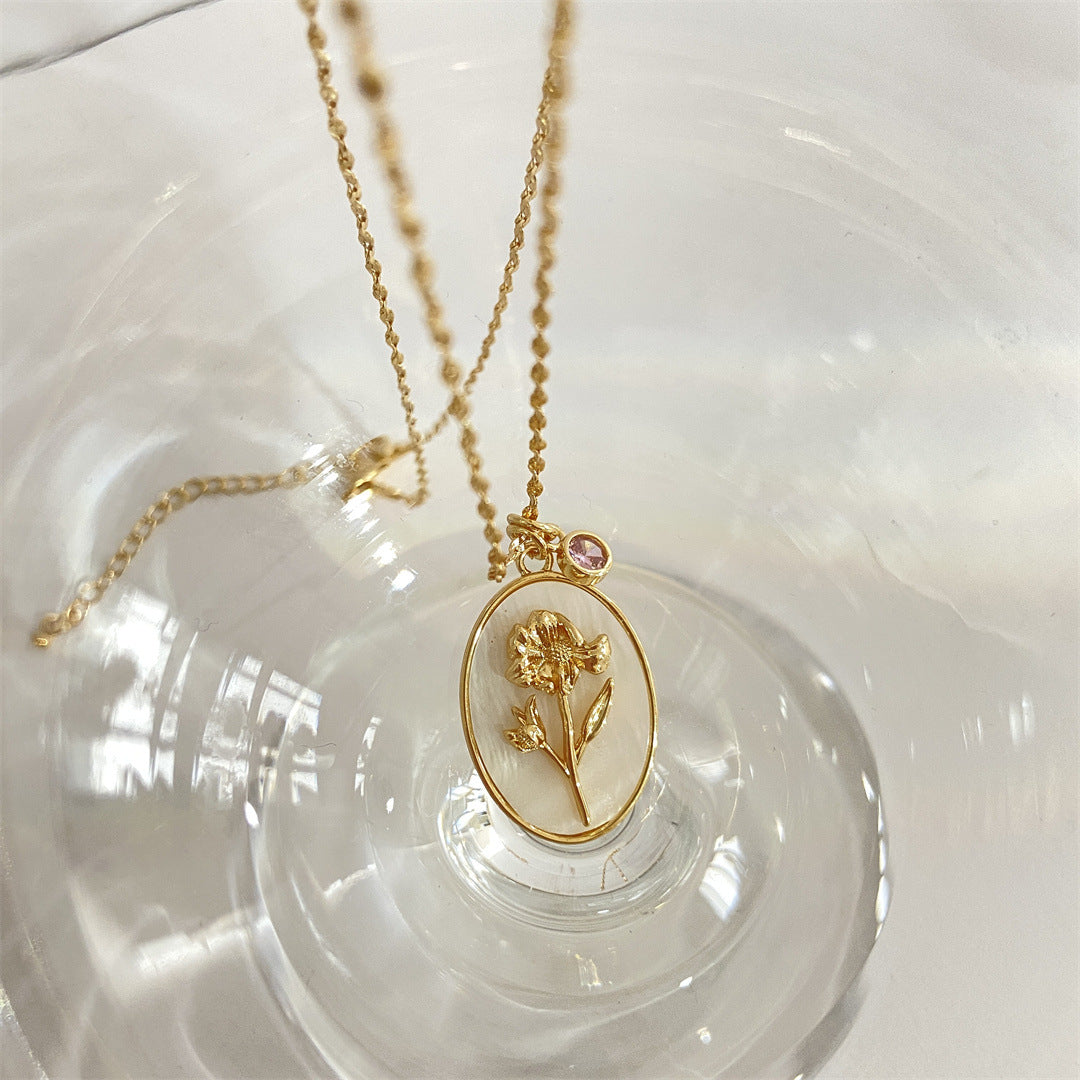 Pendentif en or avec un motif de fleur de souci gravé sur fond d'émail blanc, orné d'une petite pierre rose, faisant partie de la collection "Pendentif 12 Pierres de Naissance – Romance".