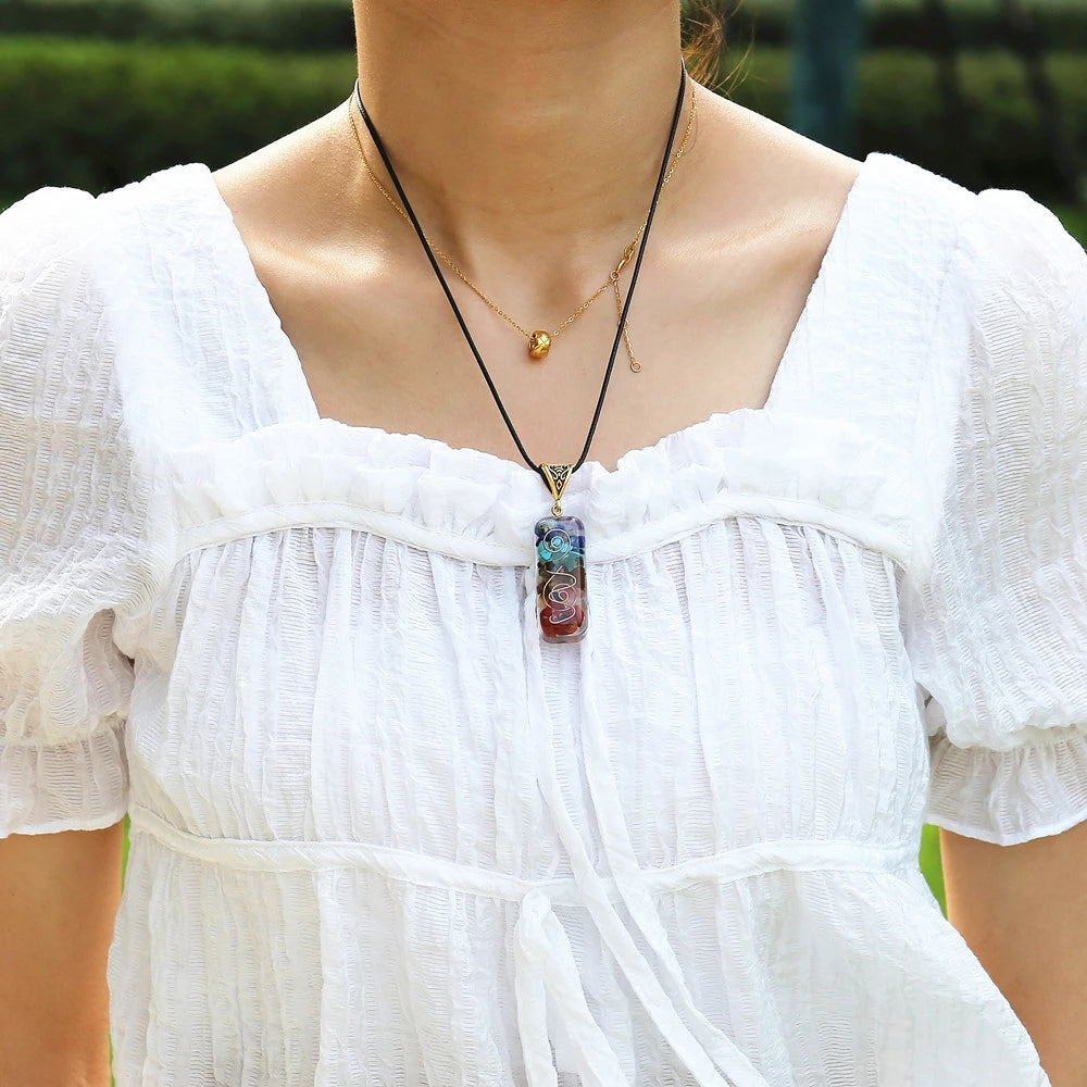 Pendentif 7 chakras en pierres naturelles multicolores, porté par une femme portant une blouse blanche.