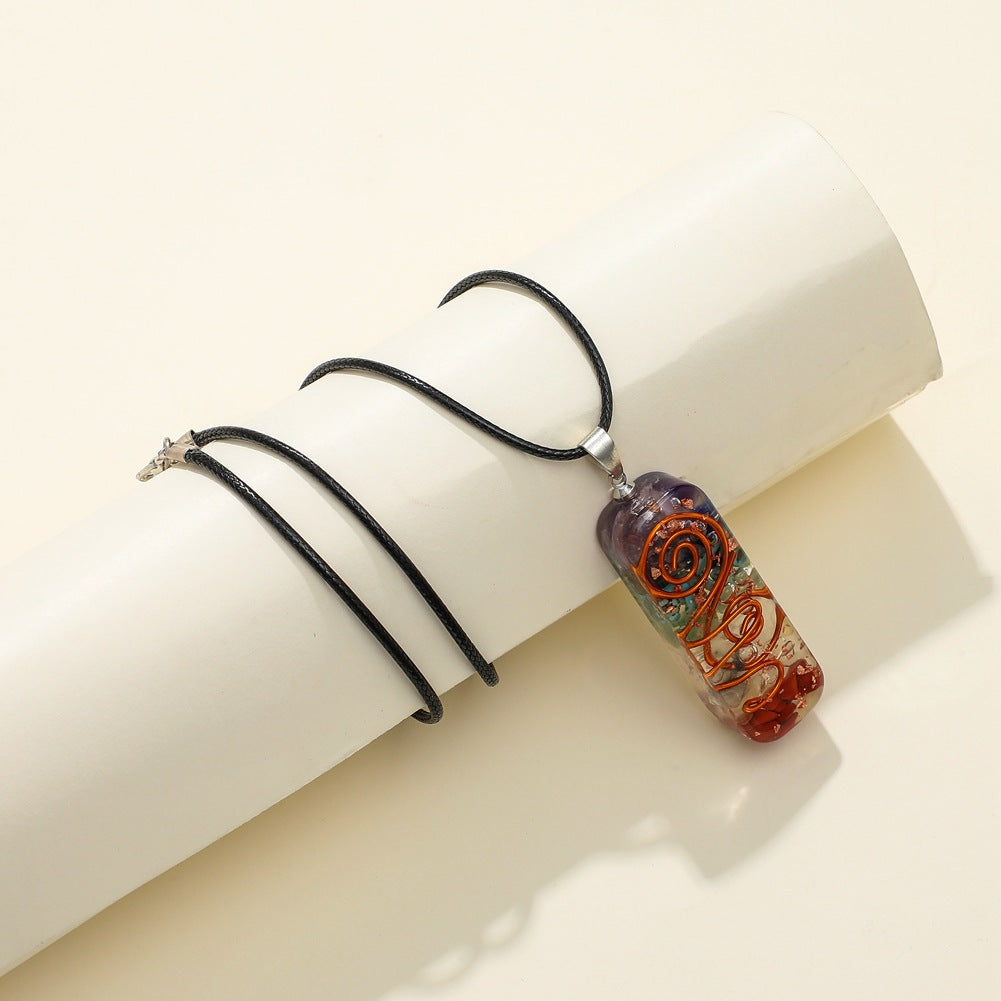 Pendentif rectangulaire 7 chakras artisanal avec des pierres naturelles colorées et un fil de cuivre torsadé, suspendu à un cordon noir.