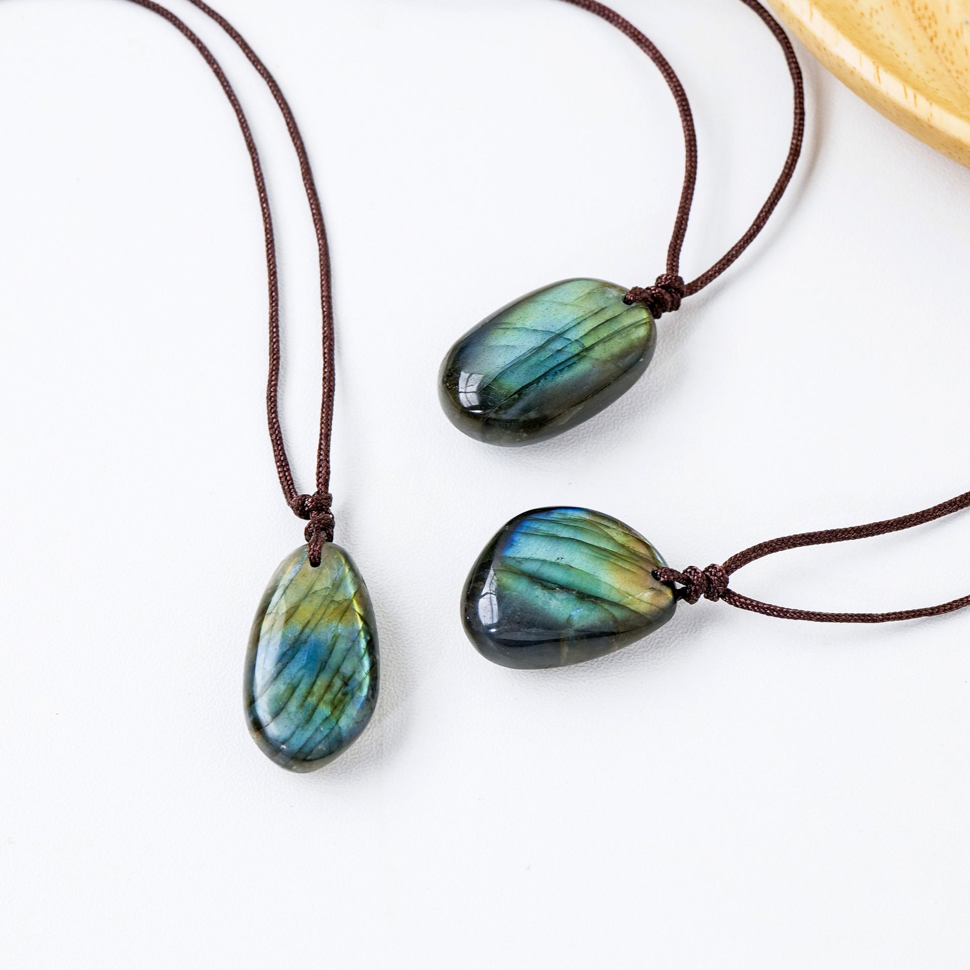 Trois pendentifs en labradorite aux reflets bleus et verts, montés sur cordon marron, sur fond blanc.