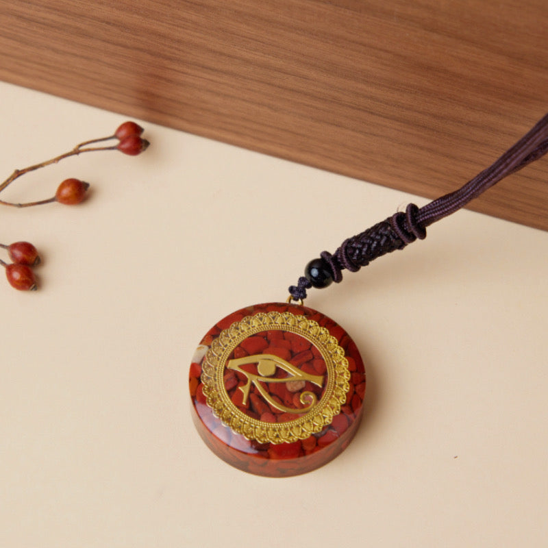 Pendentif artisanal en jaspe rouge avec symbole de l'Œil d'Horus doré, monté sur cordon tressé.