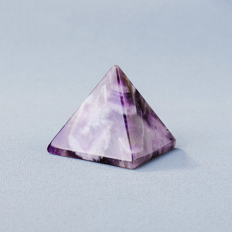 Pyramide d'améthyste polie, symbole de l'énergie positive et de la guérison spirituelle, sur fond bleu clair.