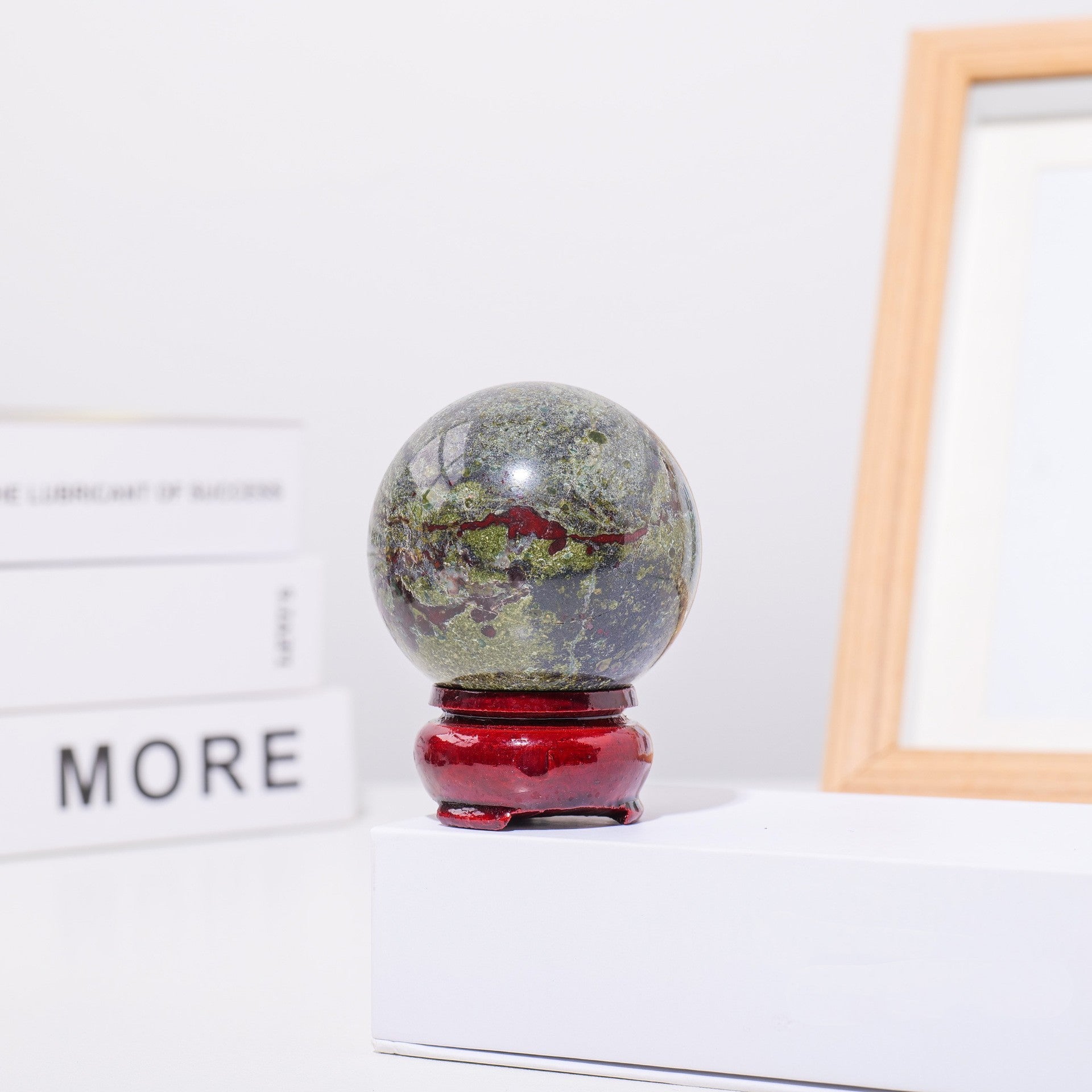 Sphère décorative "Bien-être" en pierre naturelle verte et rouge, posée sur un socle en bois rouge verni."