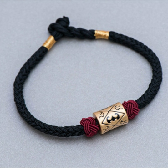 Le bracelet "Pareja" en Fil Rouge de couleur noir sur une table de couleur blanche
